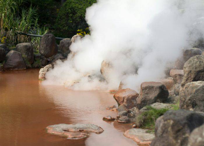 Steam rising off the surface of an onsen in Beppu; the water is a rich brown.